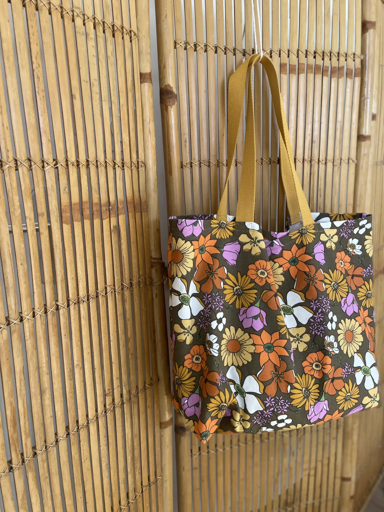 sac cabas fleuri sur fond marron en coton demi-natté. Imprimé d'inspiration seventies et flower power avec des fleurs oranges, roses et jaune. Sangle en coton moutarde.