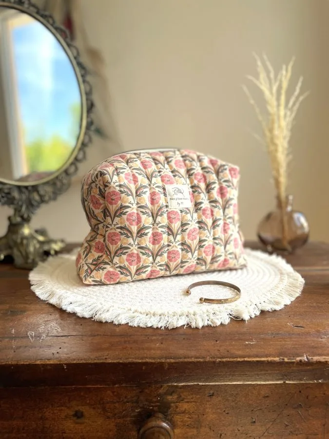 Trousse de toilette matelassée faite main. Motif fleurs indiennes dans les tons beige, orangé et kaki. Entièrement doublée en tissu mélangé de coton et lin. Passepoil doré le long du zip et noeud fantaisie accroché au curseur.